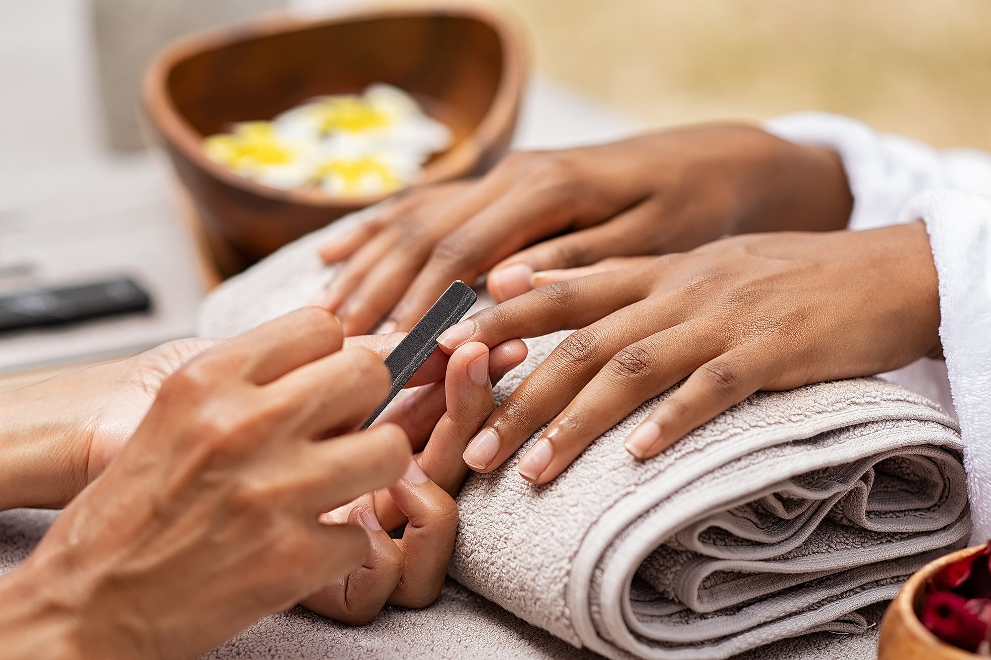 A person receiving a manicure with a nail file on a towel-covered surface.