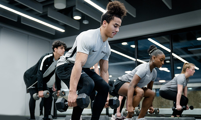 People performing dumbbell exercises in a gym.