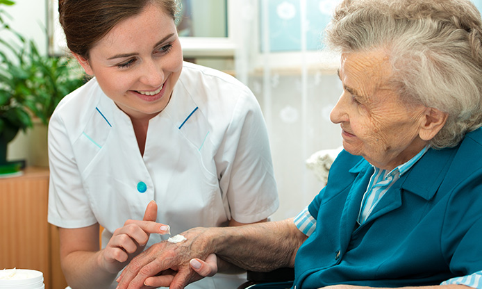 Nurse applying cream to the hands of an elderly person in a wheelchair.