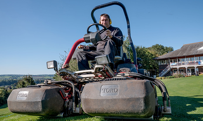 Person operating a large Toro ride-on lawn mower on a sunny day with clear skies.