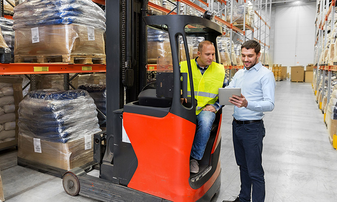 Two workers with a forklift in a warehouse, one seated on the forklift and the other standing with a tablet.