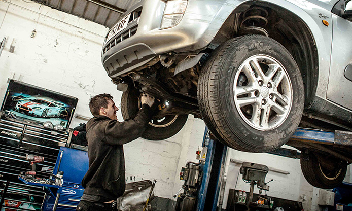 Mechanic working on SUV raised on a lift in a garage.