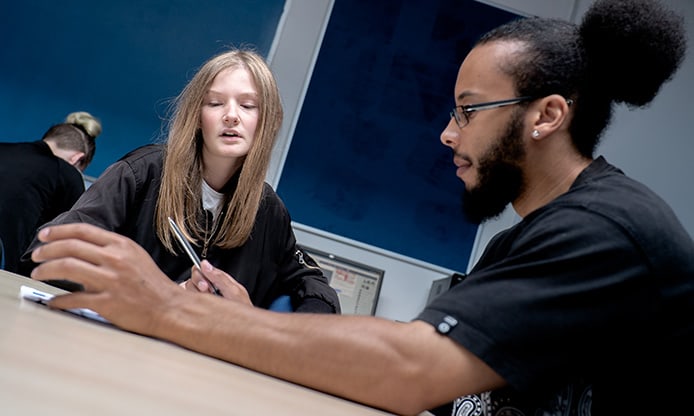 Two people in a meeting room with computers and documents on the table.