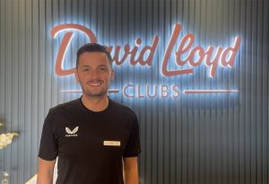 Person in black shirt with "Castore" logo, standing in front of "David Lloyd Clubs" sign.