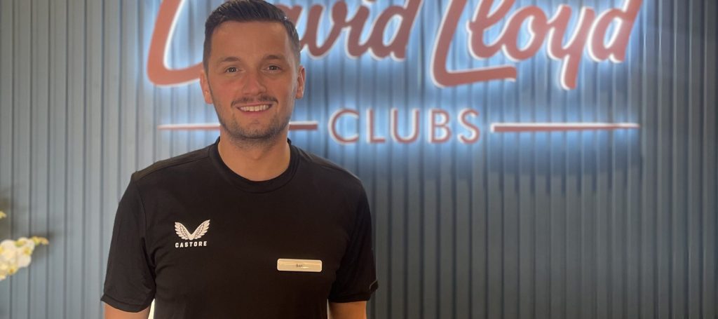 Person in black shirt with "Castore" logo, standing in front of "David Lloyd Clubs" sign.