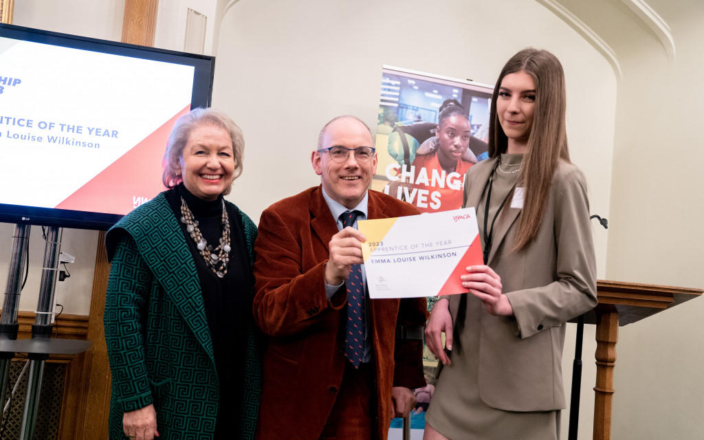 Three people standing with an award certificate, in front of a presentation screen.