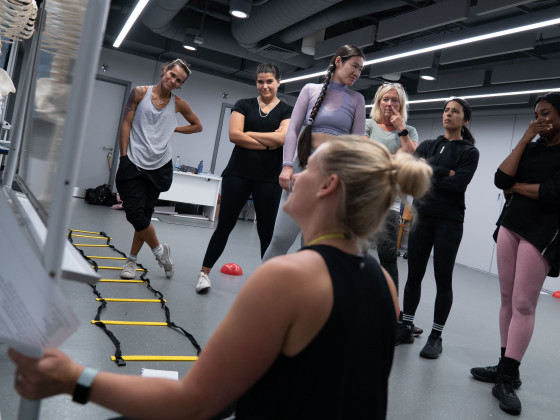 Group of people stretching in an indoor gym with exercise equipment on the floor.