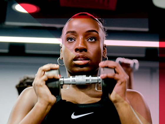 Person lifting weights at a gym, wearing a Nike tank top.