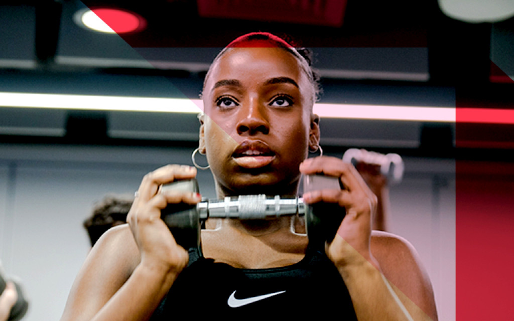 Person lifting weights at a gym, wearing a Nike tank top.