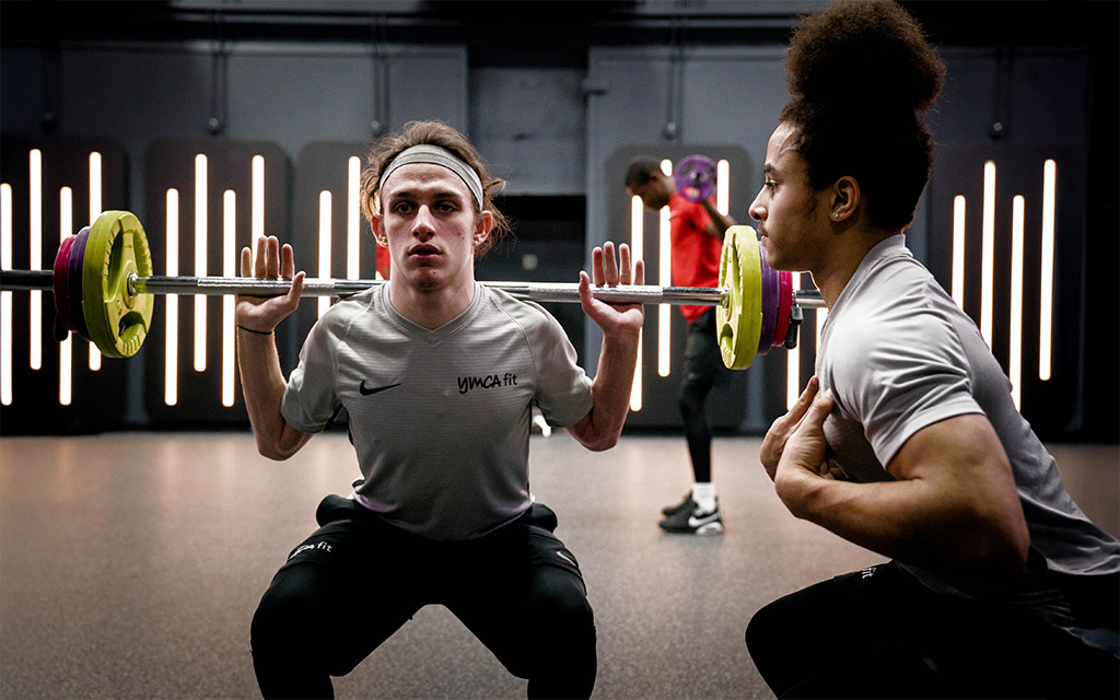 Two people performing squats with barbells in a gym with neon lights in the background.