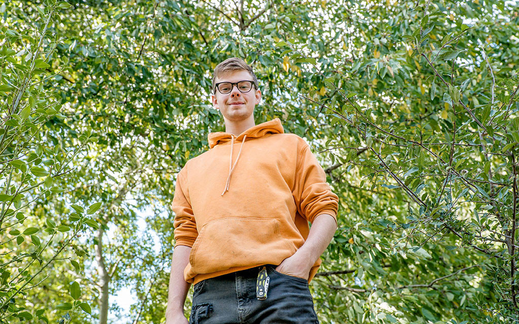 Person in orange hoodie standing among green trees.