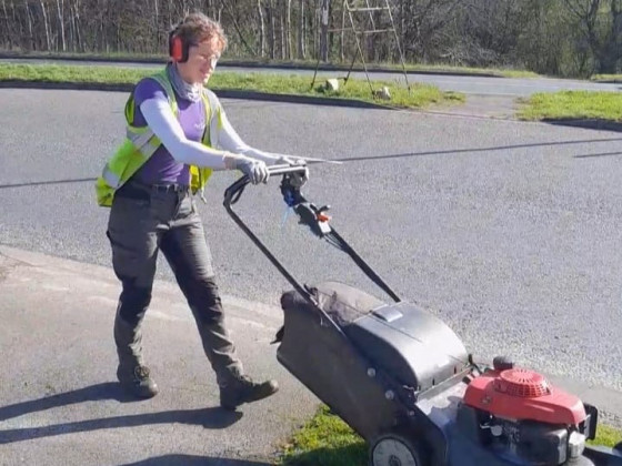 Person in high-visibility vest using a lawn mower on a sunny day.