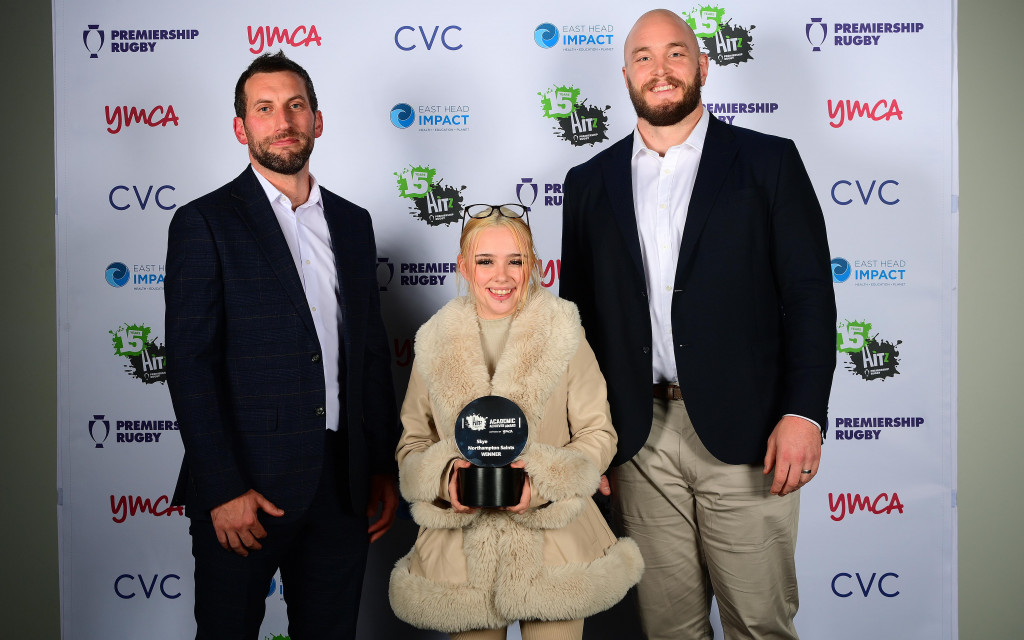 Three people posing with an award in front of a sponsor backdrop.