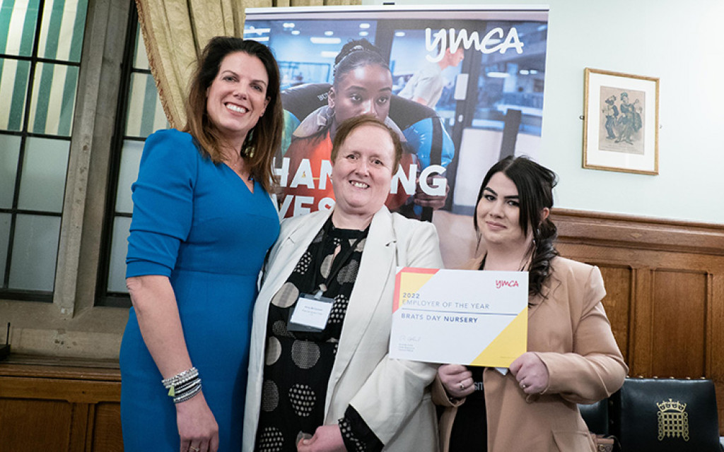 Three individuals holding an award certificate in front of a YMCA banner indoors.