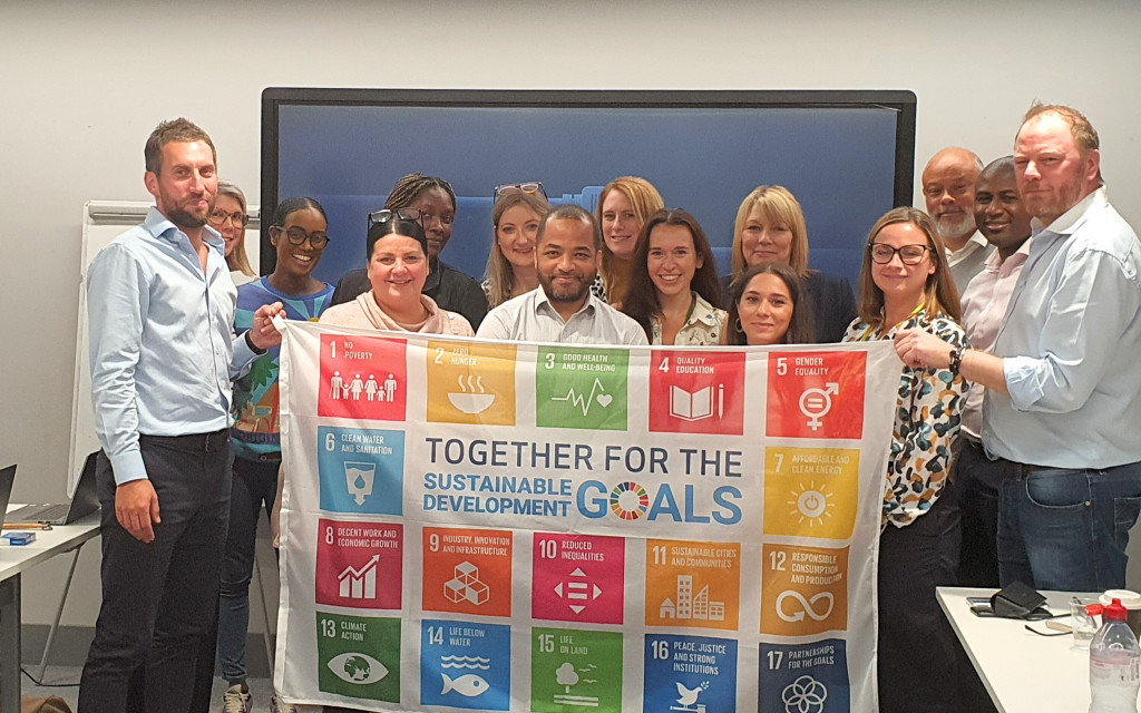 Group holding a banner with Sustainable Development Goals in an office.