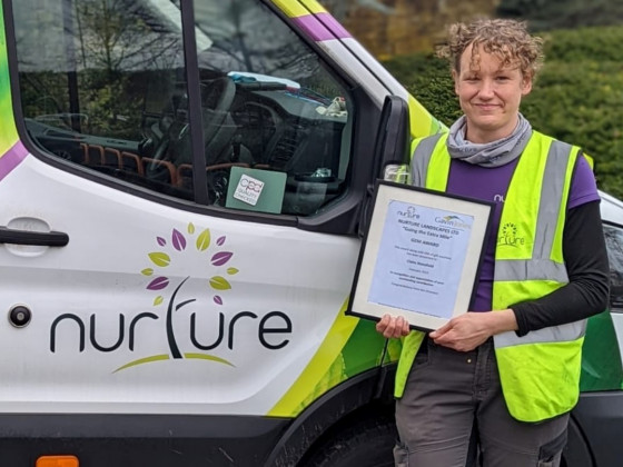 Person in high-visibility vest holding a certificate beside a van with "nurture" logo.