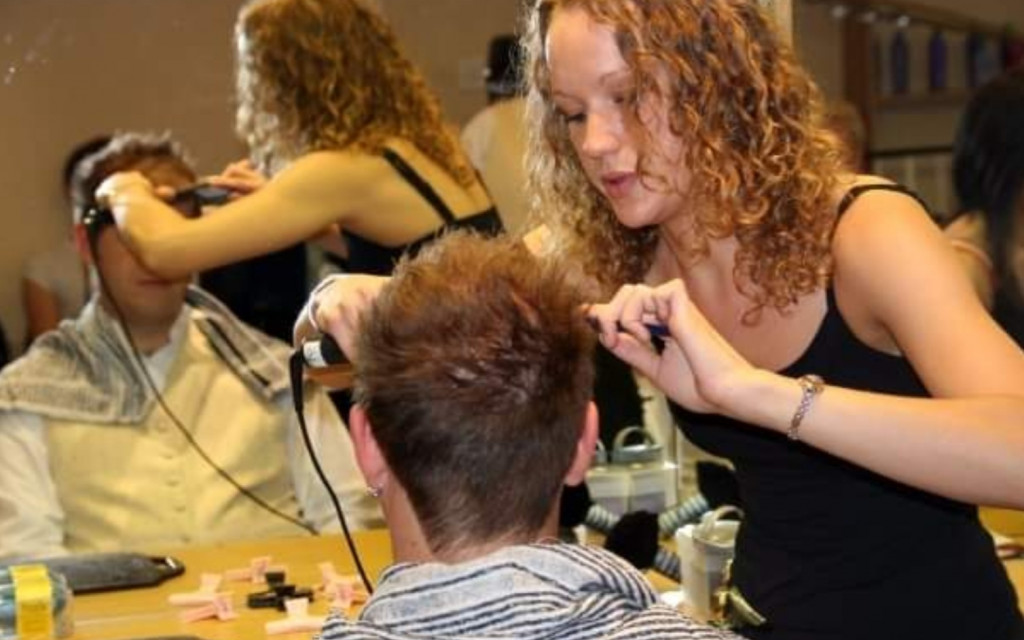 Woman styling a man's hair in a busy salon.