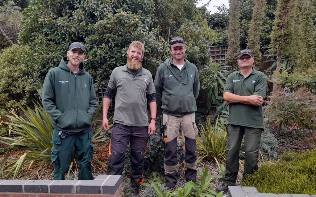 Four individuals in green workwear standing in a garden.