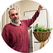 Person in a maroon sweater hanging a plant basket indoors.