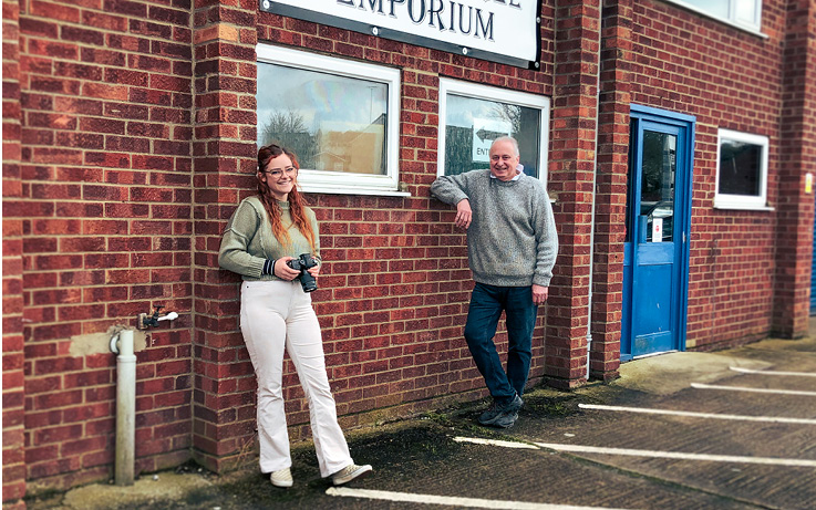 Two individuals standing outside a building with a sign "EMPORIUM" and a blue door.